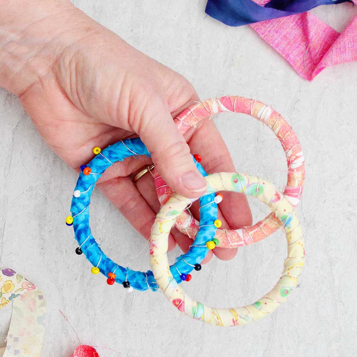 A person holding three colorful fabric BoHo bracelets, one with beads.