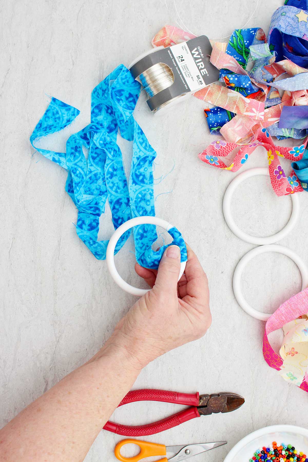A person wrapping a blue strip of fabric around a bracelet with other supplies near by.