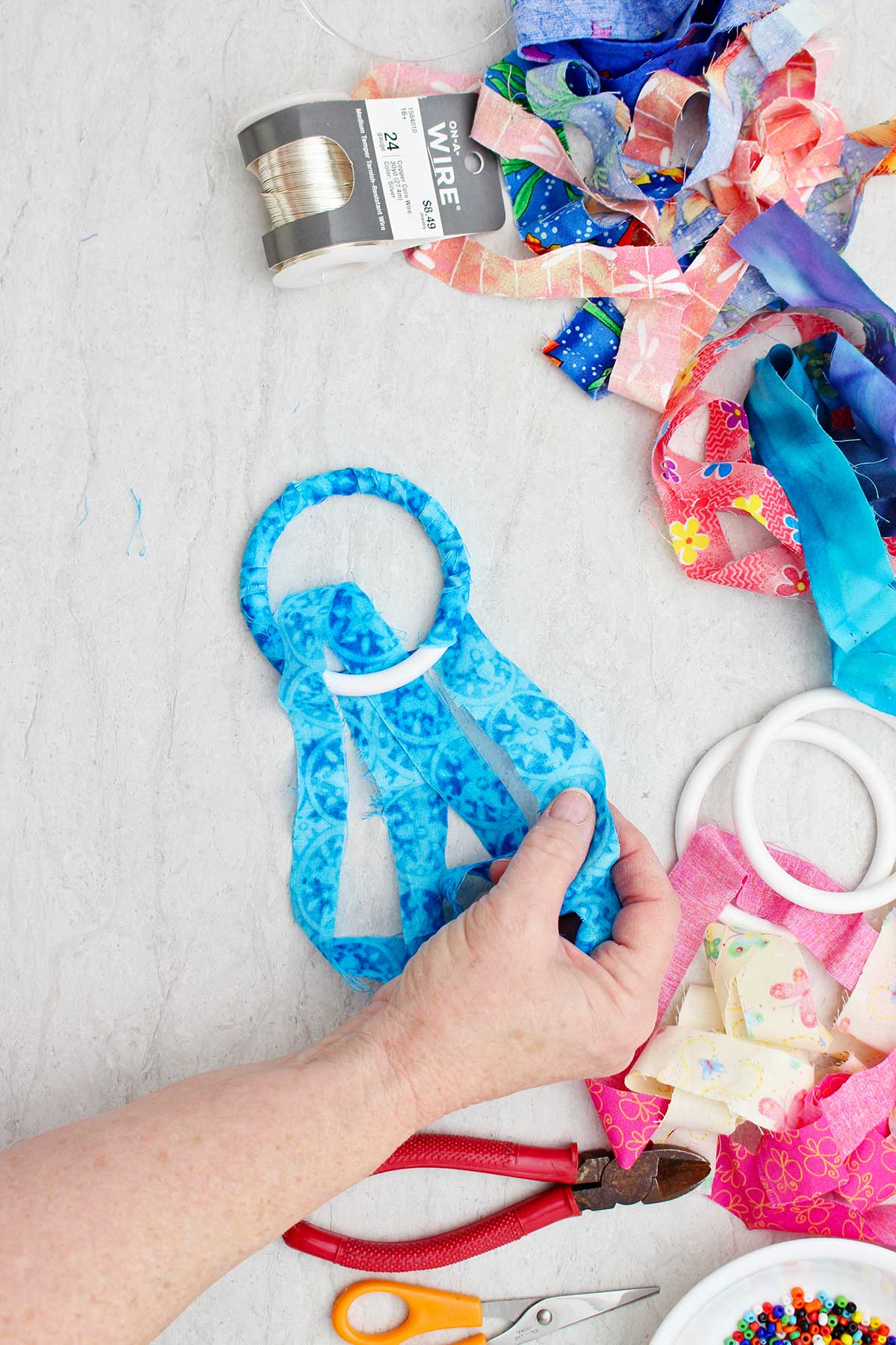 A person wrapping a blue strip of fabric around a bracelet with other supplies near by.
