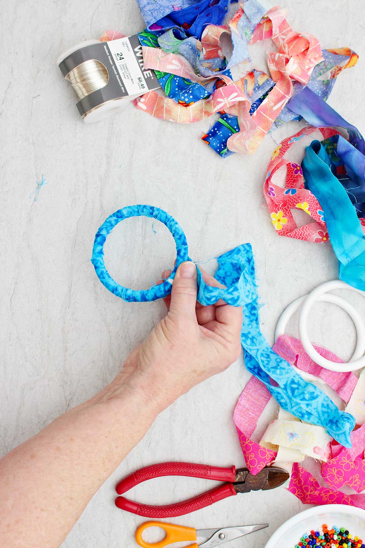 A person wrapping a blue strip of fabric around a bracelet with other supplies near by.