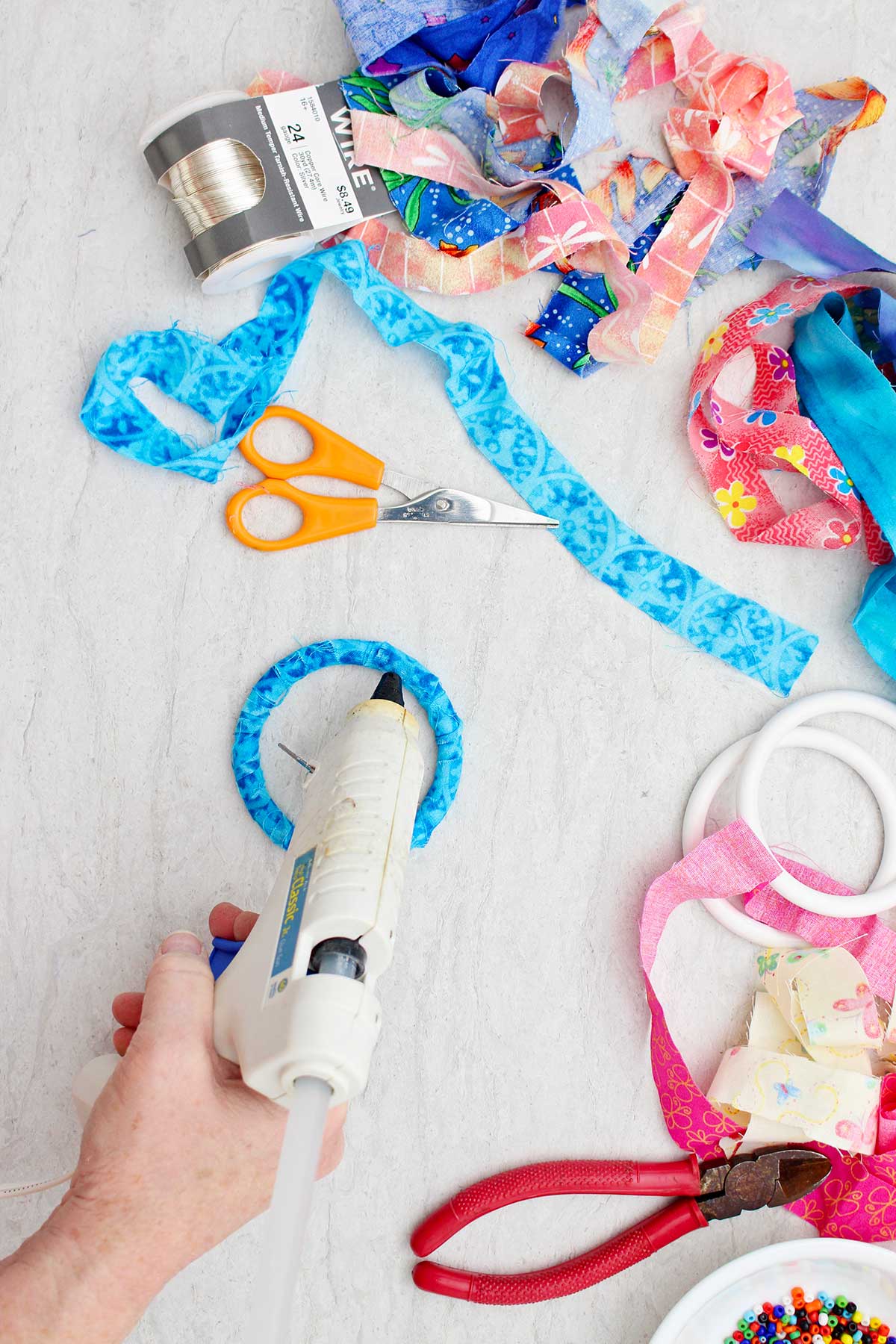 A person hot gluing the end of a blue fabric wrapped BoHo bracelet.