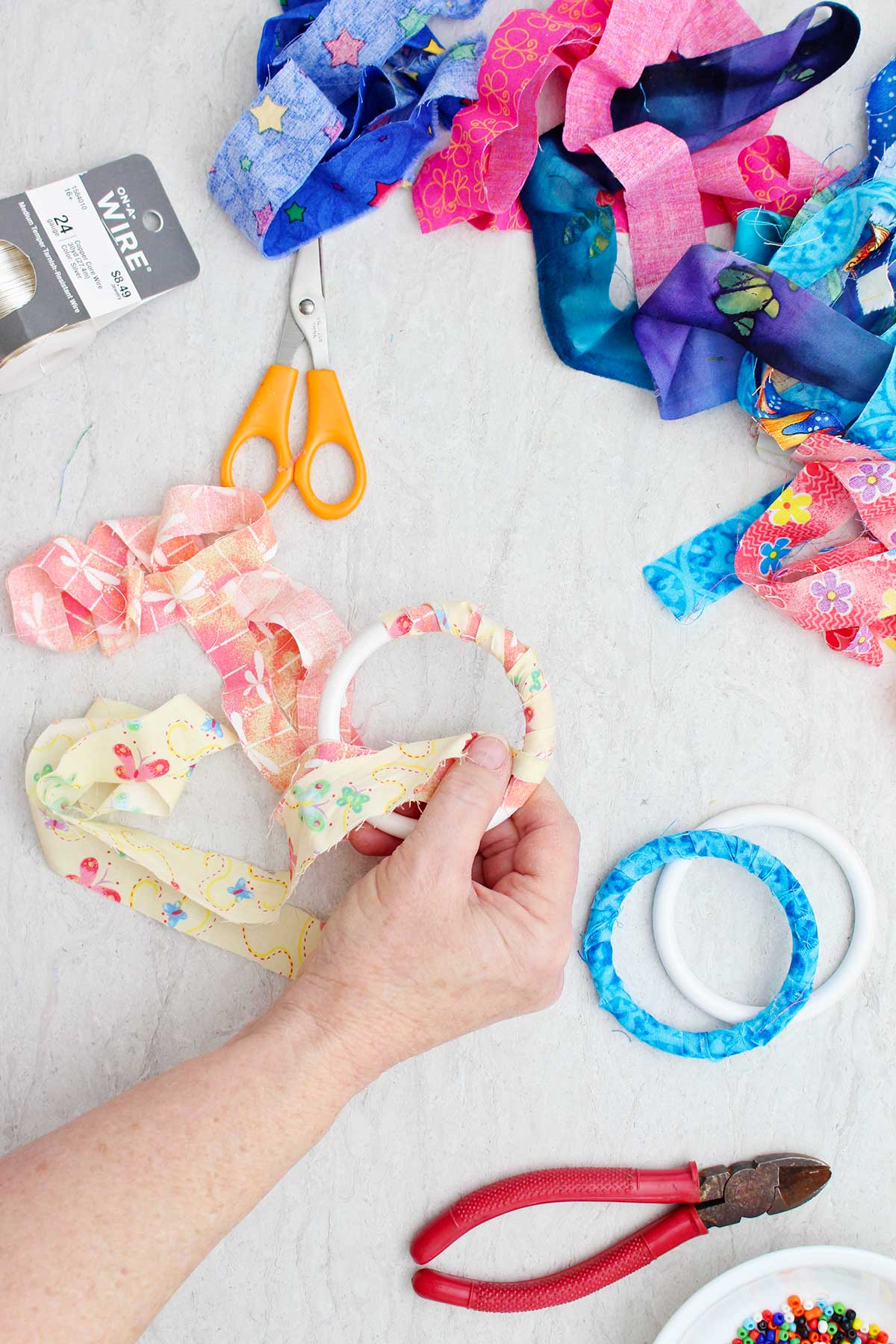 A person wrapping a yellow butterfly strip of fabric around a bracelet with other supplies near by.