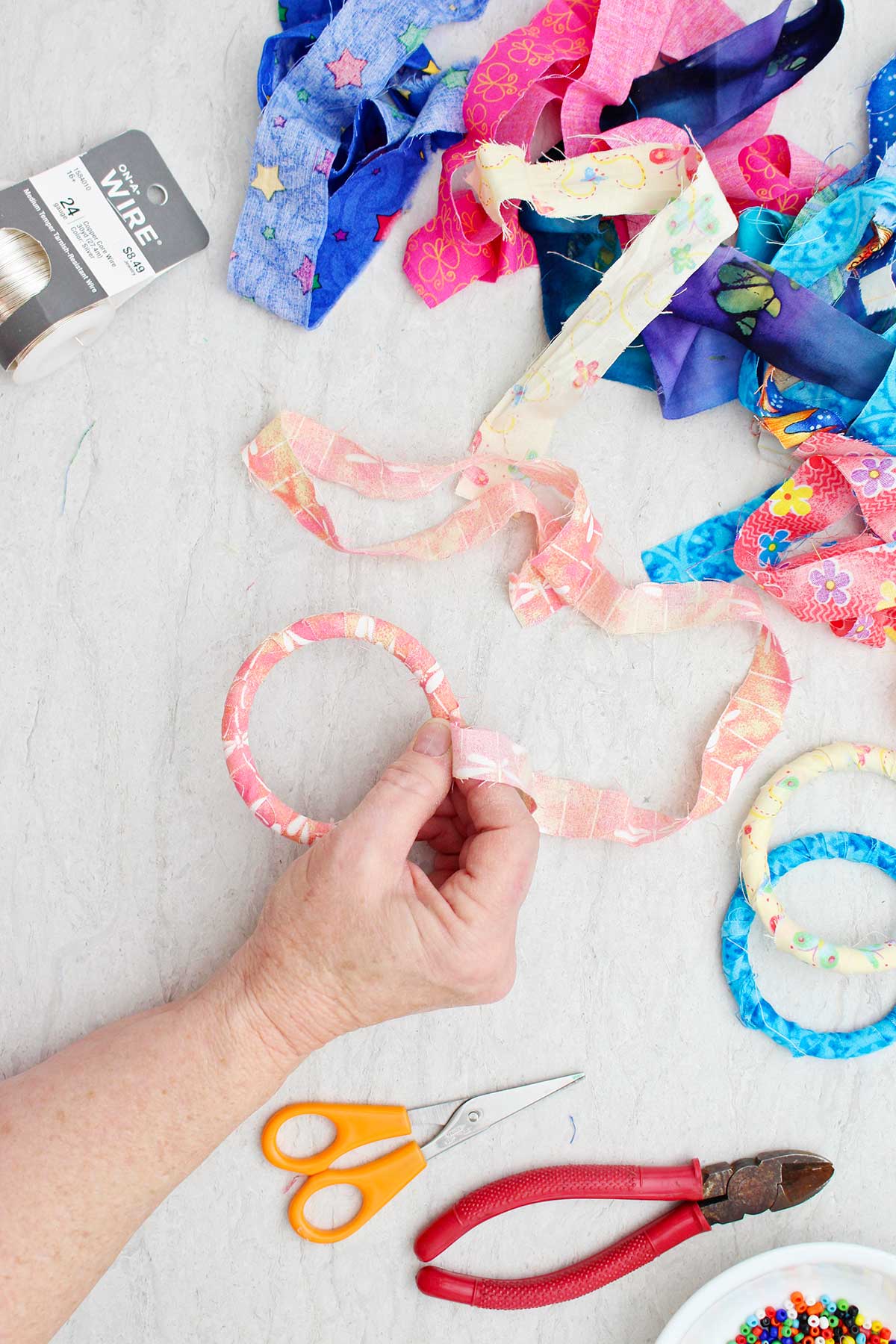 A person wrapping a peach and pink strip of fabric around a bracelet with other supplies near by.