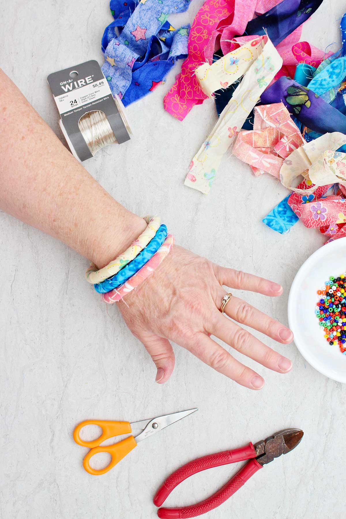 A person wearing three fabric wrapped BoHo bracelets with other scraps of colorful fabric near by.