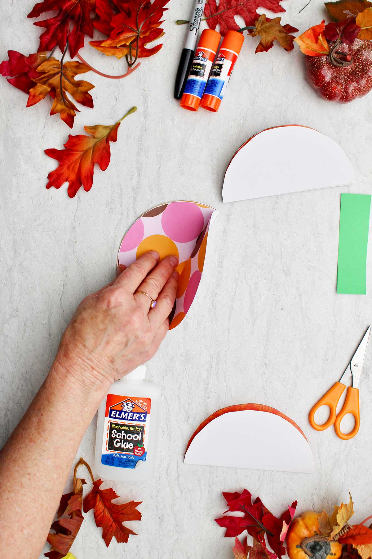 A person unfolding a patterned paper circle with colorful leaves and supplies near by.