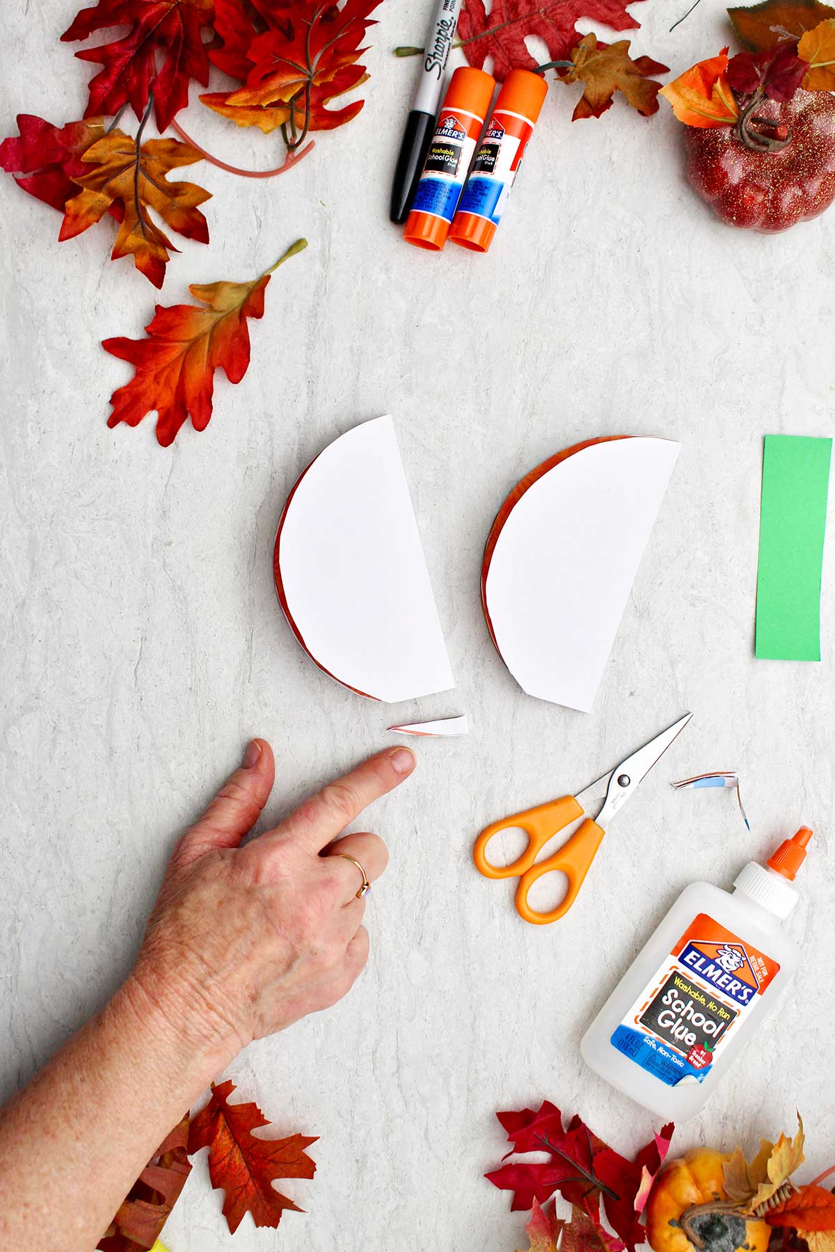 A person pointing out a small portion cut off the bottom of a half circle to make an even base for the paper pumpkin.