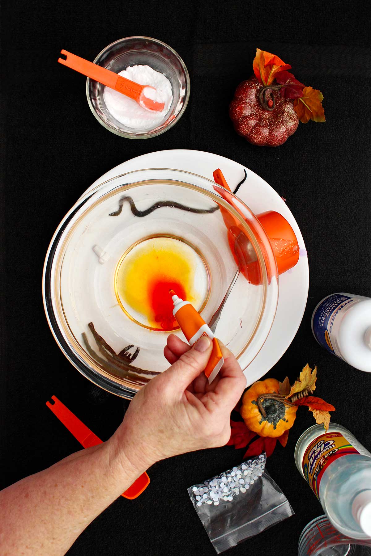 Person adding orange food coloring to a glass bowl.