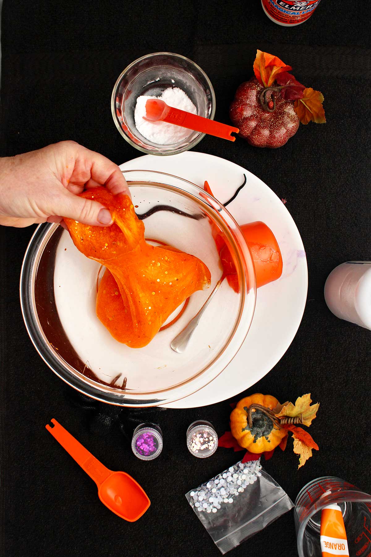 Person playing with a finished orange slime in a glass bowl.