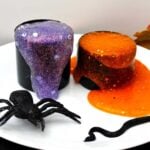 Two different spooky glittery slime recipes spilling out of their black containers with a fake spider near by.