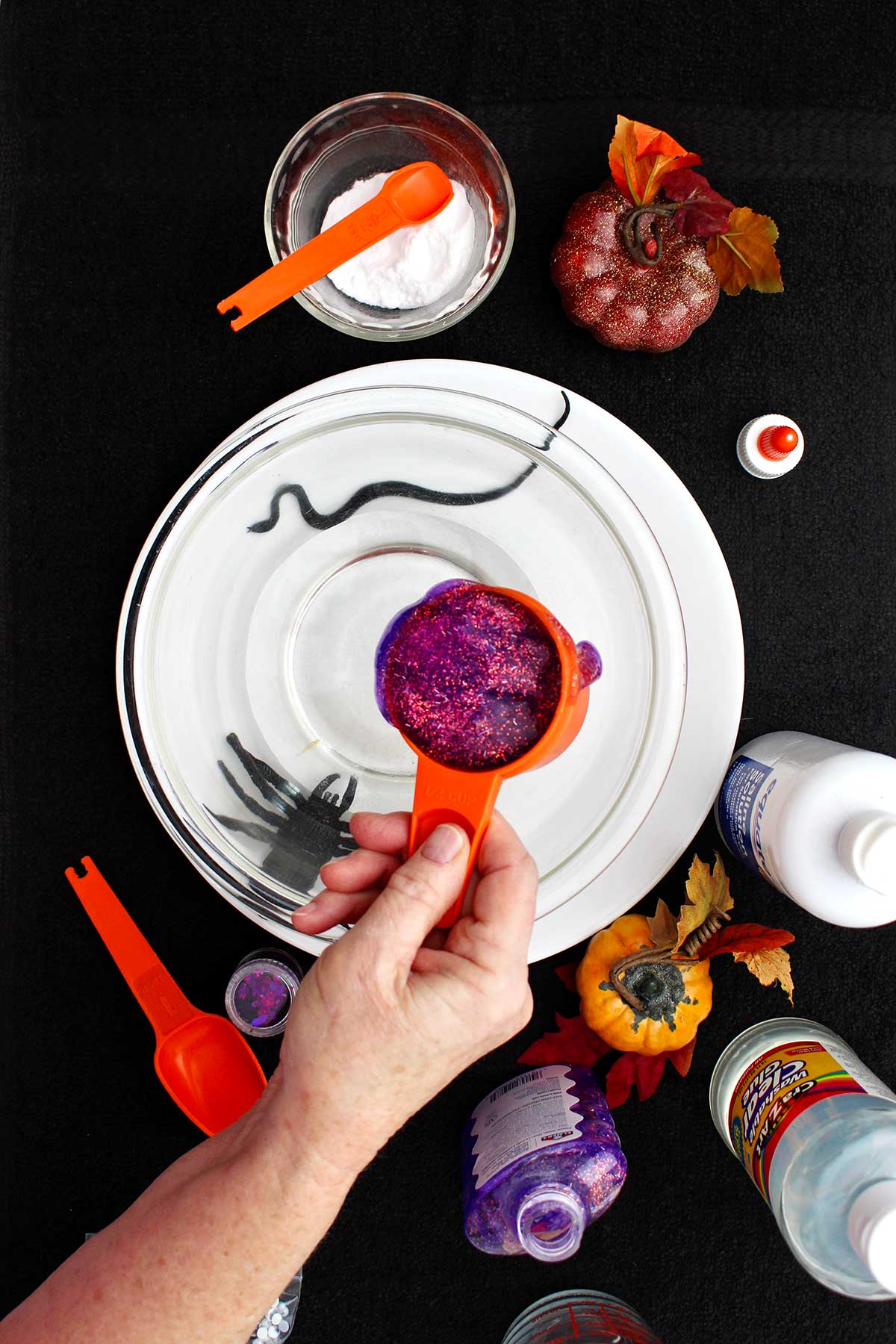 A person pouring a measuring cup of glitter glue into a glass bowl.