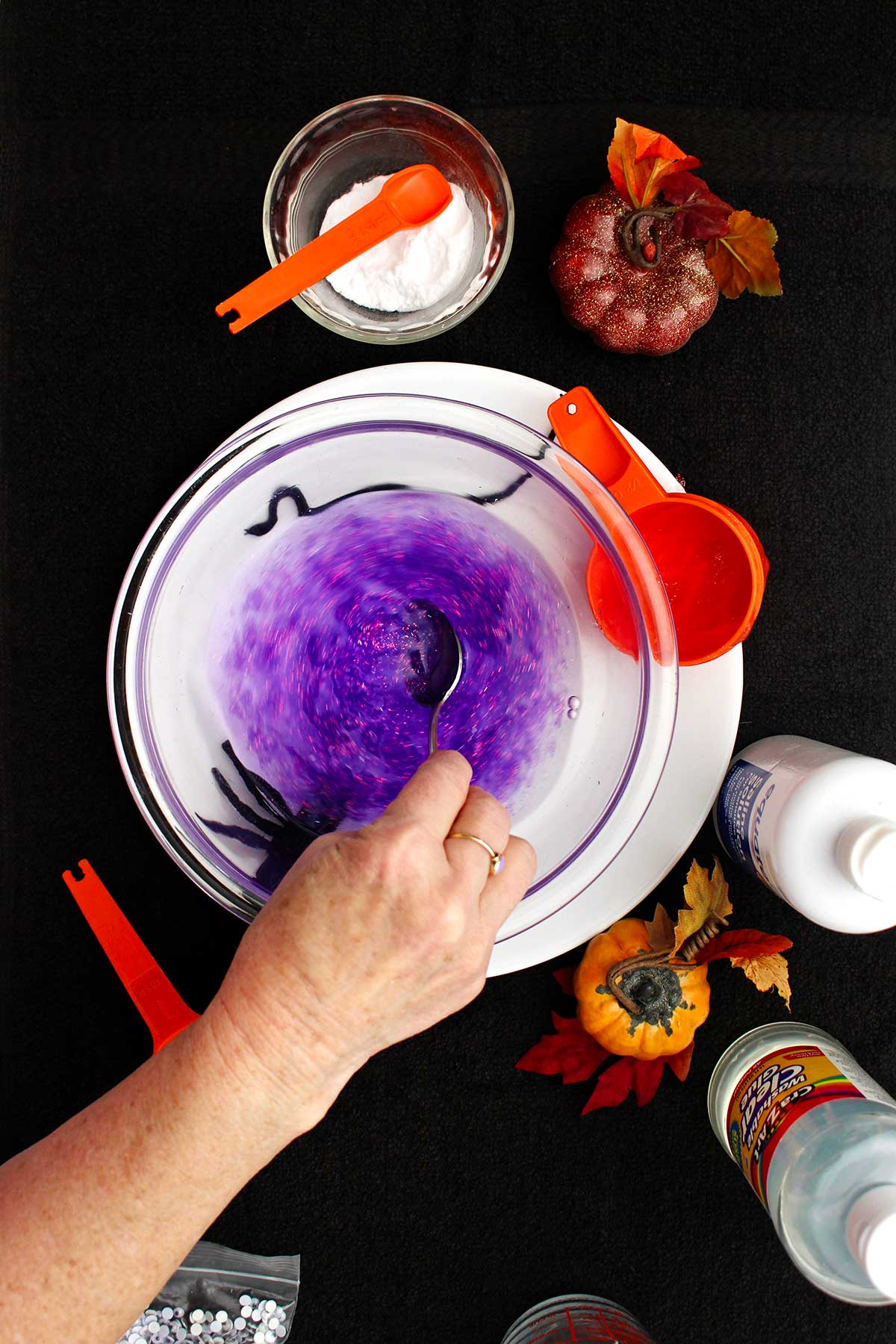 A person stirring a purple sparkly slime in a glass bowl.