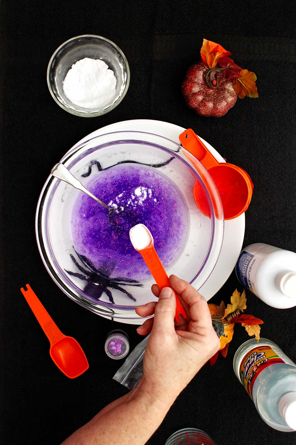 Person adding a powder ingredient into their purple slime recipe.