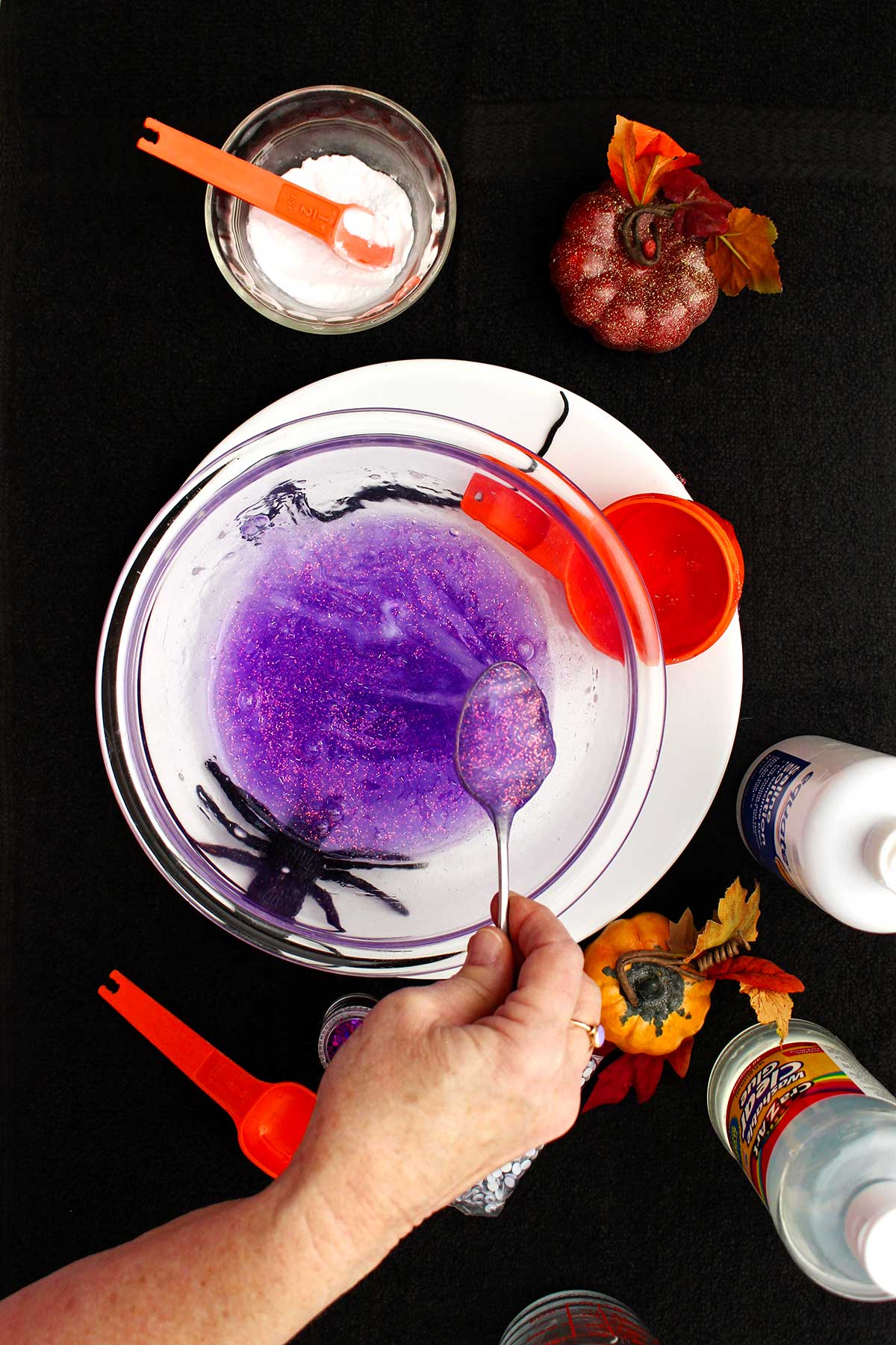 Person spooning out some purple sparkly slime from the glass bowl to show consistency.