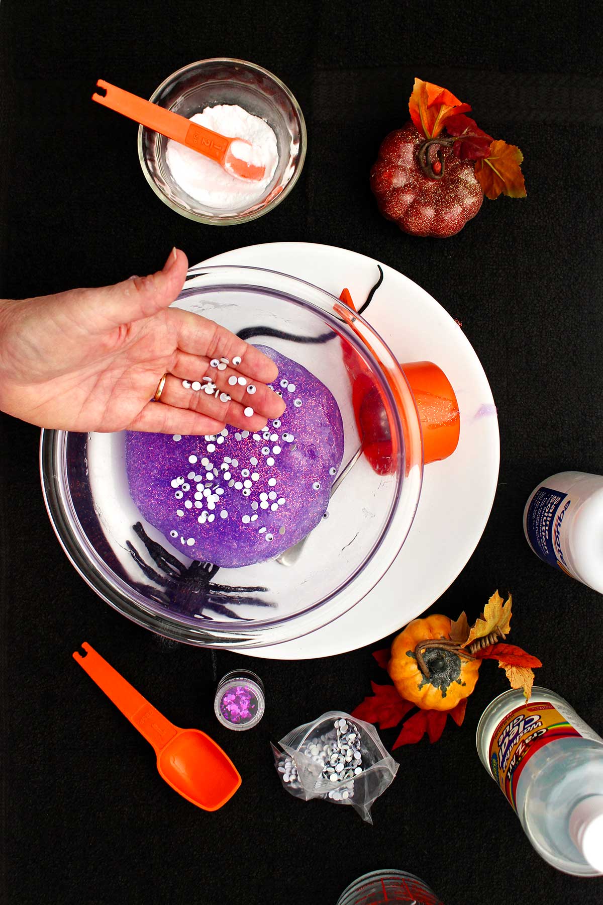 Person adding spooky mini googly eyes to their purple sparkly slime.